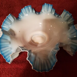 May include: A white glass bowl with blue ruffled edges. The bowl is made of milk glass and has a delicate, feminine design.