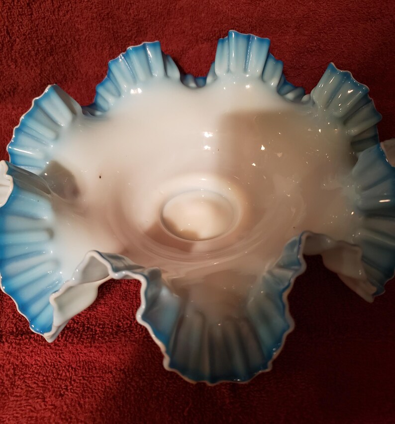 May include: A white glass bowl with blue ruffled edges. The bowl is made of milk glass and has a delicate, feminine design.