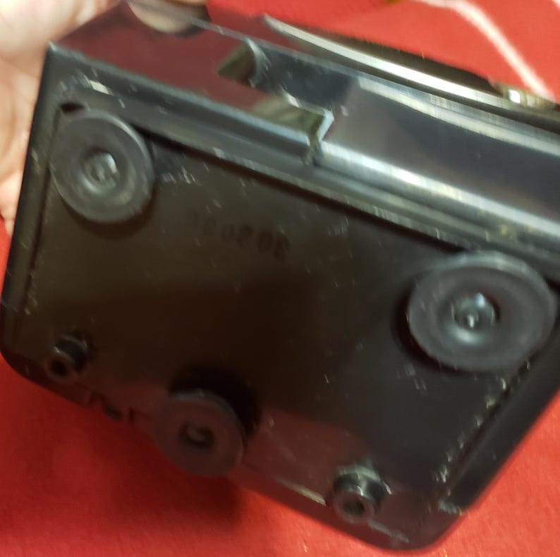 May include: A black rectangular object with four circular rubber feet. The object has a glossy finish and appears to be made of plastic. The number "30 20" is printed on the surface.