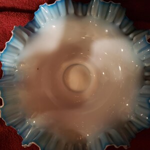 May include: A white glass bowl with a blue ruffled edge. The bowl is made of milk glass and has a scalloped edge.