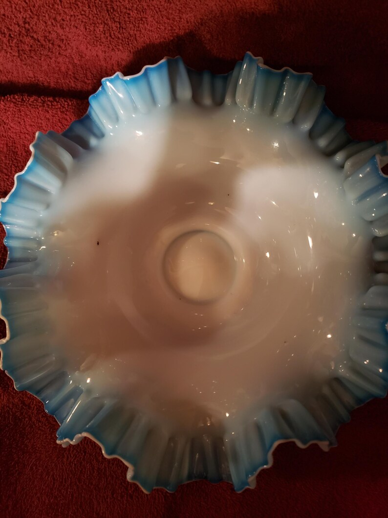 May include: A white glass bowl with a blue ruffled edge. The bowl is made of milk glass and has a scalloped edge.