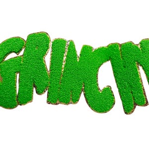 Könnte beinhalten: Grünes, strukturiertes Wort "GRINCH" mit goldenem Rand, isoliert auf weißem Hintergrund. Die Buchstaben sind in einer verspielten, abgerundeten Schriftart gehalten, die ein skurriles und festliches Thema hervorruft. Ideal für Bastelarbeiten und Dekorationen zum Thema Feiertage.