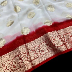 Puede incluir: Sari blanco con bordado dorado y borde rojo. El sari viene con una blusa roja a juego.