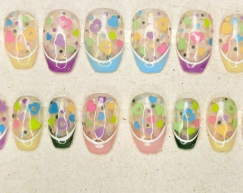 May include: Set of 20 false nails with a clear base and colorful confetti design. The nails are in a variety of shapes and sizes, with a white tip on each nail.
