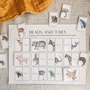 May include: A printable educational game for kids featuring a white sheet with the words "Heads and Tails" and a grid of 16 squares. Each square has a different animal head or tail, with the words "Head" or "Tail" written below. The game includes 16 cards with animal illustrations, each card showing either the head or tail of the animal.
