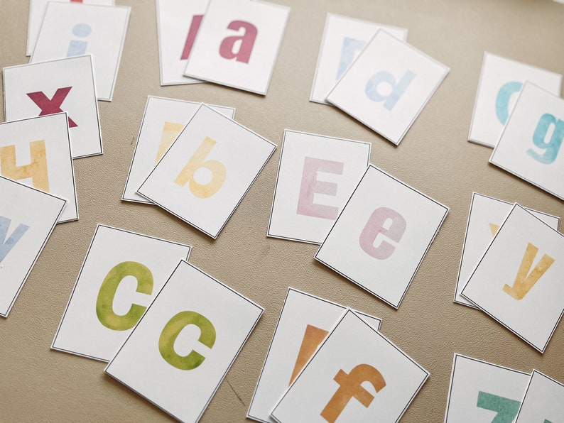 May include: A set of alphabet letter cards with watercolor-style lettering. The letters are printed on white cardstock with a black border. The letters are in various colors, including blue, green, yellow, pink, and red.