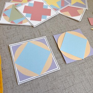 May include: A collection of colorful geometric paper cutouts. The designs include squares, circles, and cross shapes in pastel colors like blue, peach, and lavender. The cutouts are arranged on a gray surface.