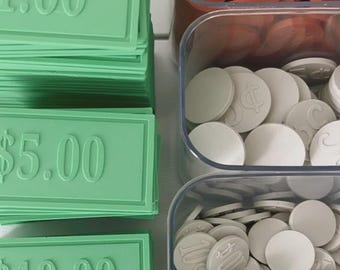 Könnte beinhalten: Grünes Spielgeld aus Kunststoff in den Werten 1,00 $, 5,00 $ und 10,00 $. Klare Kunststoffbehälter enthalten weiße und orangefarbene Spielmarken, einige mit Dollarzeichen und Zahlenaufdrucken. Ideal für Brettspiele oder Lernspiele.