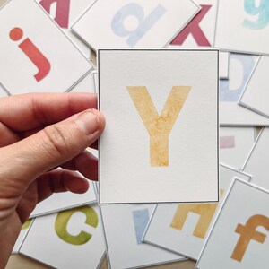 May include: A white card with a black border, featuring the letter Y in a yellow watercolor style.