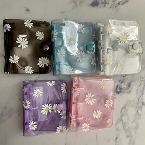 May include: Five clear plastic binders with daisy patterns. The binders are in different colors: brown, blue, white, purple, and pink.