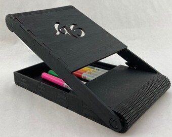 May include: A black wooden box with a hinged lid. The lid has a cut-out design of the number "16". The box is open and contains several colored markers.