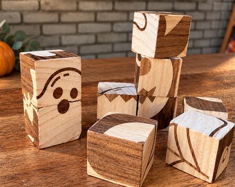 May include: A set of light and dark brown wooden blocks featuring laser-engraved ghost designs. The blocks are arranged in various configurations, with some stacked to form complete ghost figures and others placed individually to show patterns.
