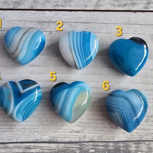 Può includere: Sei pietre a forma di cuore con vari motivi blu, bianchi e grigi. Ogni pietra ha una superficie lucida e liscia. Le pietre sono numerate da 1 a 6 e sono esposte su una superficie di legno chiaro.