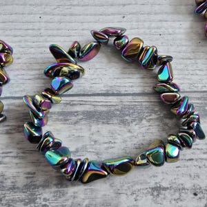Op de afbeelding: Iridescent hematiet stenen armbanden. Elke armband heeft gepolijste, onregelmatig gevormde stenen in tinten paars, blauw, groen en goud. De stenen zijn aan elkaar geregen, waardoor een uniek en opvallend accessoire ontstaat.