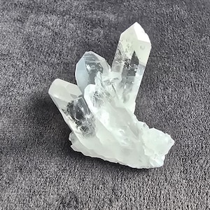 Könnte beinhalten: Eine Ansammlung von klaren, durchscheinenden Quarzkristallen mit scharfen, spitzen Enden. Das Mineralexemplar besteht aus mehreren miteinander verbundenen Spitzen, die aus einer gemeinsamen Basis wachsen und natürliche Facetten sowie Einschlüsse aufweisen.