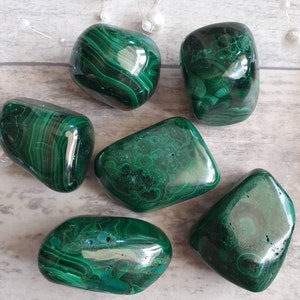 Puede incluir: Un conjunto de piedras de malaquita pulidas, mostrando un color verde intenso con intrincados patrones arremolinados. Las piedras varían en tamaño y forma, con una superficie brillante y reflectante. Las formaciones naturales crean una estética única, ideal para coleccionistas o entusiastas de los cristales.