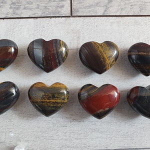 Op de afbeelding: Acht gepolijste hartvormige stenen met een mix van kleuren, waaronder rood, bruin, geel en grijs. De stenen zijn gerangschikt in twee rijen van vier, waarbij hun unieke patronen en texturen worden getoond.