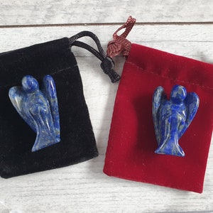 Könnte beinhalten: Zwei Engel-Figuren aus Lapislazuli, eine in einem schwarzen Samtbeutel und die andere in einem roten Samtbeutel. Die Engel sind mit detaillierten Flügeln und Gewändern geschnitzt. Die Beutel haben Kordelverschlüsse.