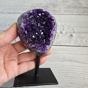 Può includere: Geode di ametista lucidata, con un interno di cristallo viola intenso. La geode è montata su un supporto in metallo nero, creando un contrasto sorprendente. Pietra naturale decorativa.