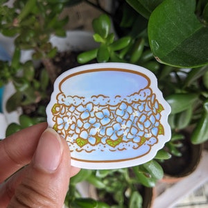 May include: A blue and gold sticker with a white background featuring a stylized illustration of a cake decorated with blue flowers.