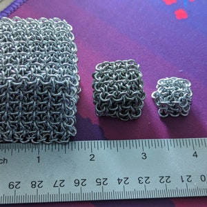 May include: Three silver chainmail squares of different sizes, measured in inches on a ruler. The largest square is about 2 inches wide, the middle square is about 1 inch wide, and the smallest square is about 0.5 inches wide.