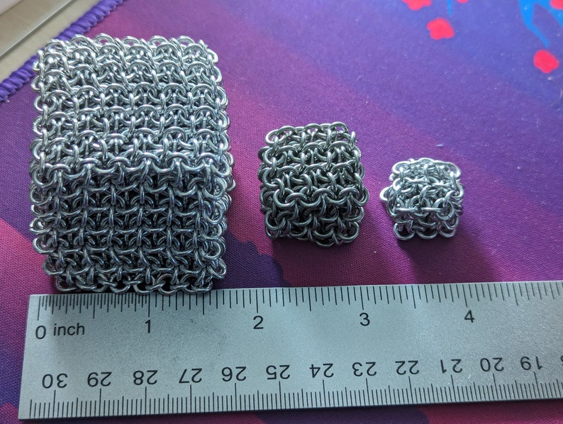 May include: Three silver chainmail squares of different sizes, measured in inches on a ruler. The largest square is about 2 inches wide, the middle square is about 1 inch wide, and the smallest square is about 0.5 inches wide.