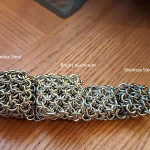 May include: Four chainmail squares, two made of stainless steel and two made of bright aluminum. The squares are arranged in a row from left to right, with the stainless steel squares on the ends and the aluminum squares in the middle.