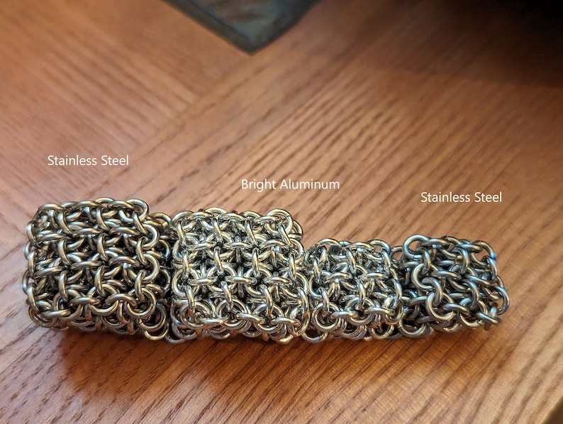 May include: Four chainmail squares, two made of stainless steel and two made of bright aluminum. The squares are arranged in a row from left to right, with the stainless steel squares on the ends and the aluminum squares in the middle.