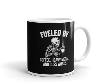 May include: Black coffee mug with a white skeleton holding a coffee cup and the text "Fueled by Coffee, Heavy Metal and Cuss Words".