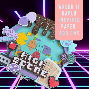 May include: A set of paper craft cutouts inspired by the Wreck-It Ralph movie. The set includes a Pac-Man character, ghosts, candy, a high score sign, and a fist. The cutouts are on a blue background with a pink and purple grid pattern.