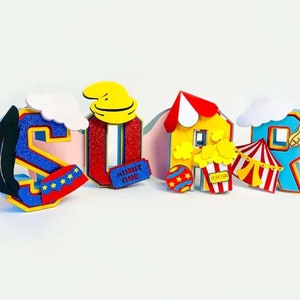 Puede incluir: Un conjunto de letras coloridas que deletrean "SOIR" decoradas con elementos de temática circense. Las letras están hechas de espuma y tienen un acabado brillante. Las decoraciones incluyen un sombrero de payaso, una carpa, palomitas de maíz y un boleto que dice "ADMIT ONE".