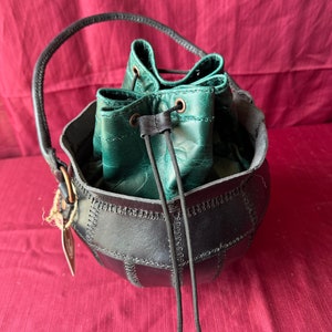May include: A black leather drawstring bag with a green leather lining. The bag has a stitched design and a black drawstring.