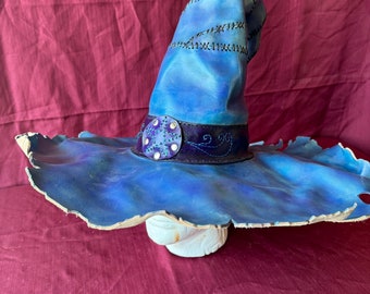 May include: A blue leather wizard hat with a wide brim and a decorative buckle. The hat is stitched with black thread and has a tie.