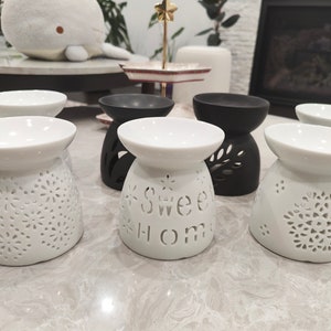 May include: Five ceramic oil diffusers, two black and three white. The white diffusers have intricate floral designs and the text "Sweet Home" is etched into one of the white diffusers.