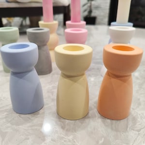May include: A set of ten candle holders in various pastel colors, including light blue, pink, yellow, and orange. The candle holders are made of a textured material and have a simple, modern design.