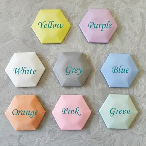 May include: Eight hexagonal tiles, each painted a different color and labeled with the color name in teal text. The colors are yellow, purple, white, grey, blue, orange, pink, and green.