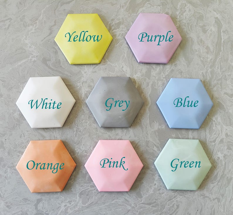May include: Eight hexagonal tiles, each painted a different color and labeled with the color name in teal text. The colors are yellow, purple, white, grey, blue, orange, pink, and green.