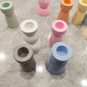 May include: A collection of colorful candle holders made of ceramic. The holders are in various shapes and sizes, including round, square, and cylindrical. The colors include light blue, light green, light pink, white, and gray.