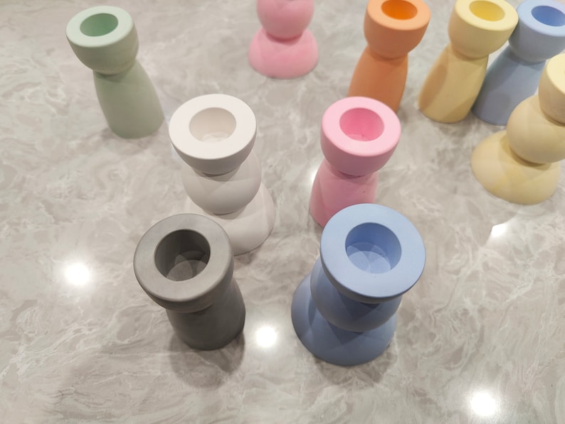 May include: A collection of colorful candle holders made of ceramic. The holders are in various shapes and sizes, including round, square, and cylindrical. The colors include light blue, light green, light pink, white, and gray.