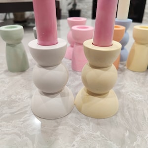 May include: A set of six candle holders in various pastel colors, including light green, pink, yellow, and blue. The candle holders are made of ceramic and have a simple, modern design.