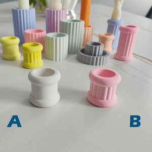 May include: Two small white and pink candle holders with a fluted design. The holders are on a white surface. The white holder is labeled "A" and the pink holder is labeled "B".