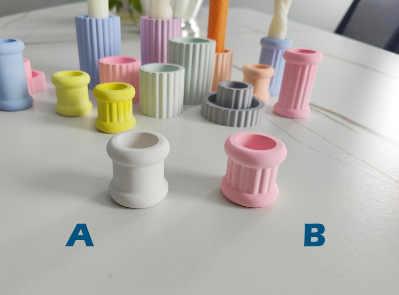 May include: Two small white and pink candle holders with a fluted design. The holders are on a white surface. The white holder is labeled "A" and the pink holder is labeled "B".