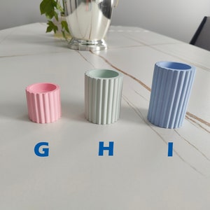 May include: Three small decorative containers with ribbed sides. The container on the left is pink, the middle container is light green, and the container on the right is light blue.