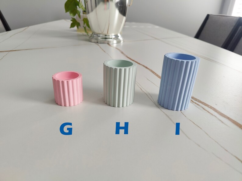May include: Three small decorative containers with ribbed sides. The container on the left is pink, the middle container is light green, and the container on the right is light blue.