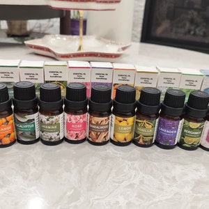 Könnte beinhalten: Ein Set mit 15 kleinen Glasflaschen mit schwarzen Kappen, jede gefüllt mit ätherischem Öl. Die Flaschen sind in einer Reihe auf einer weißen Oberfläche angeordnet. Die Etiketten auf den Flaschen zeigen verschiedene Farben und Designs, darunter florale Muster, Zitrusfrüchte und abstrakte Designs. Die Etiketten enthalten auch die Namen der ätherischen Öle, wie "Pfefferminze", "Orange", "Eukalyptus", "Jasmin", "Rose", "Sandelholz", "Zitrone", "Vanille", "Lavendel", "Bergamotte", "Eukalyptus", "Ozean" und "Weihrauch".