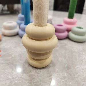 May include: A set of five candle holders in various pastel colors. The candle holders are made of ceramic and have a stacked, rounded design. The candle holders are arranged on a white surface.