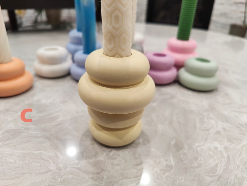 May include: A set of five candle holders in various pastel colors. The candle holders are made of ceramic and have a stacked, rounded design. The candle holders are arranged on a white surface.