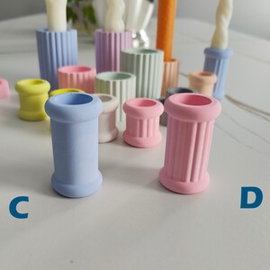 May include: A set of 10 colorful candle holders in various pastel colors, including light blue, pink, yellow, and green. The holders are made of ceramic and have a fluted design. The holders are arranged in a group on a white surface.
