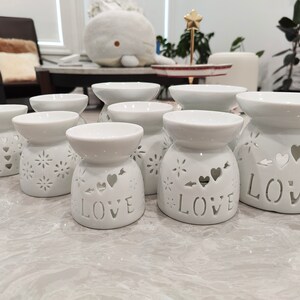 May include: Eight white ceramic oil diffusers with intricate designs. Some diffusers feature the word "LOVE" and heart cutouts.