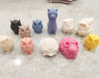 May include: A collection of 11 animal-shaped candles, including owls, a llama, a hedgehog, and a sheep. The candles are made of wax and are painted in various colors, including pink, yellow, white, and blue.